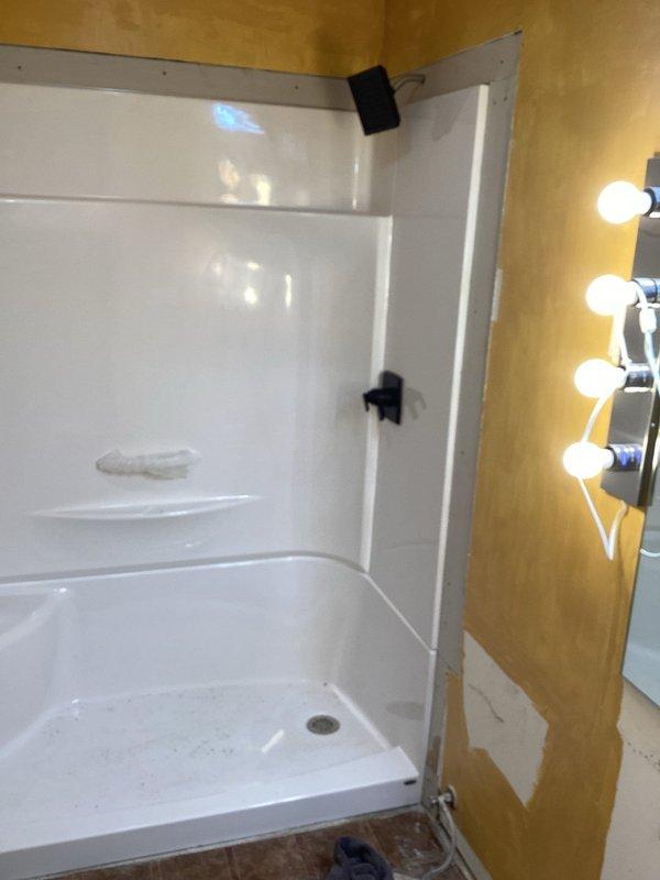 Two technicians completed a full-day installation of a new one-piece fiberglass shower enclosure in a bathroom corner. The scope included setting the molded shower base with integrated pan and drain assembly, securing the three-panel surround system with mounting hardware, reworking the drain connection to align with the new fixture, and installing drywall around the perimeter of the shower stall to enclose the unit. The drywall finishing, trim work, and shower fixture installation were left for subsequent completion.