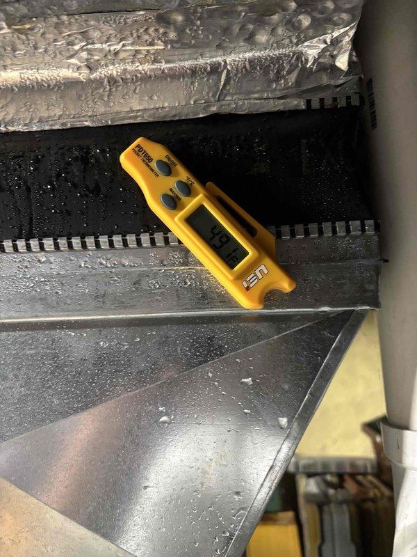 Completed follow-up maintenance visit after original planned maintenance was not finished by previous technician. Accessed HVAC unit and inspected evaporator coil assembly, noting active condensation present on coil fins and drain pan, indicating normal system operation. Documented temperature readings using calibrated digital thermometer, recording 64.88°F at evaporator coil surface. Verified proper drainage with visible moisture collection in metal drain pan. Inspected heat exchanger fins for cleanliness and airflow obstruction, observing accumulated dust and dirt on coil surfaces and base components. System components including ductwork, evaporator coils, and drain pan confirmed to be intact and functioning. Photographic documentation captured for service records showing coil condition, temperature measurements, and condensation patterns.