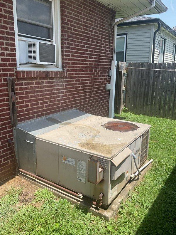Conducted replacement estimate for aging package unit experiencing refrigerant leaks. System displayed significant exterior corrosion, rust staining around fan assembly, and deteriorated metal casing with paint failure. Homeowner currently utilizing portable air conditioning units due to system failure. Documented unit condition with photographs showing extensive weathering on outdoor equipment positioned on concrete pad against brick structure. Provided comprehensive replacement options as repair was not requested due to extent of system degradation.