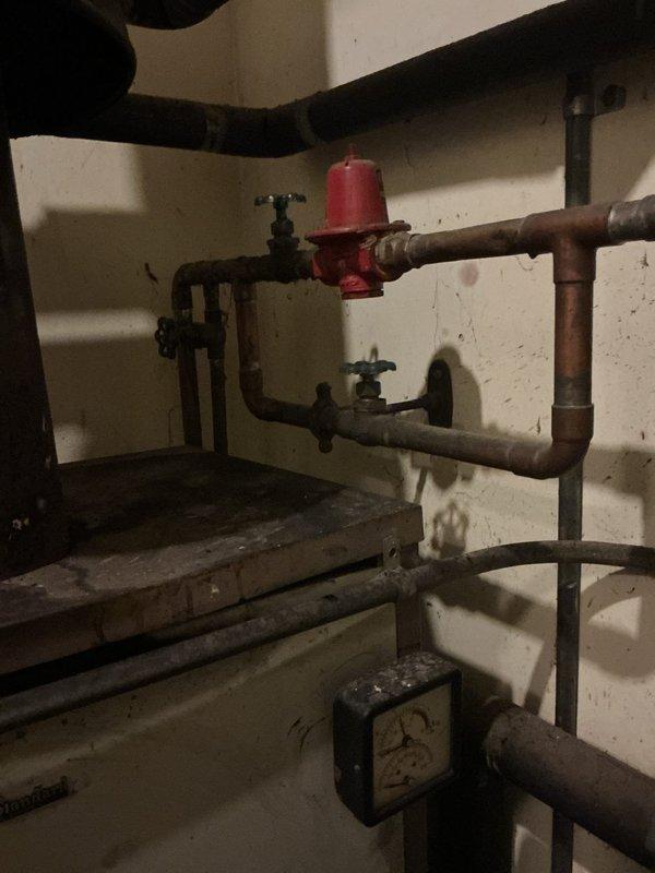 Conducted comprehensive assessment of existing 60+ year old boiler system for replacement estimate. Documented current plumbing infrastructure including aged copper piping with visible oxidation, pressure regulation equipment, and multiple valve assemblies. Evaluated mechanical room conditions and existing pipe configurations to determine scope of work required for new boiler installation. Photographed current system components including corroded metal fittings, black iron piping, and water distribution connections to provide accurate replacement specifications and identify necessary upgrades to bring system up to current code standards.