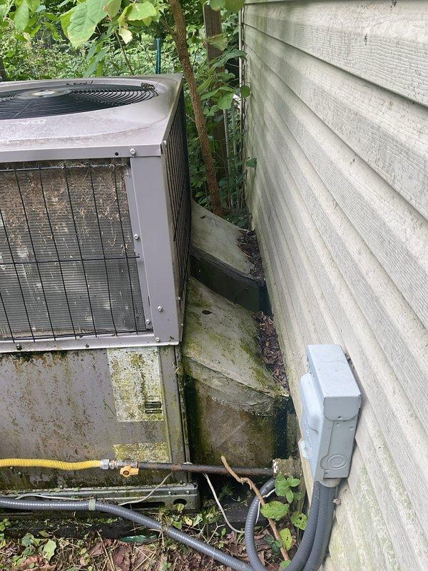 Conducted comprehensive HVAC system evaluation for heating and cooling replacement estimate on a packaged unit installation serving a 1001-1599 square foot residential structure utilizing natural gas energy source. Assessed existing exterior-mounted packaged unit positioned on deteriorated concrete pad with significant algae and moss accumulation, noted inadequate clearances due to vegetation encroachment, and documented weathered electrical disconnect, compromised refrigerant line insulation, and deteriorating foundation access panel with organic growth. Provided detailed photographic documentation of current equipment condition, installation deficiencies, and site constraints to develop accurate replacement specifications for new packaged HVAC system.
