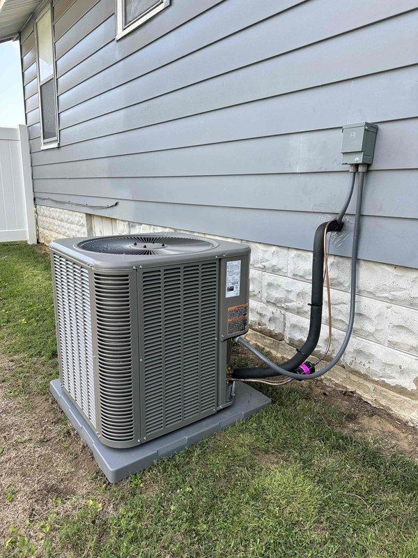 Completed installation of a 2.5-ton, 15.5 SEER Lennox air conditioning system with matching evaporator coil at residential property. The outdoor condenser unit (model 13ACX-LQ30-230A03) was positioned on a concrete pad against the building exterior with proper clearance for airflow and service access, electrical disconnect box mounted on siding with conduit run to unit, and refrigerant line set connected with insulated wrap at penetration point.
