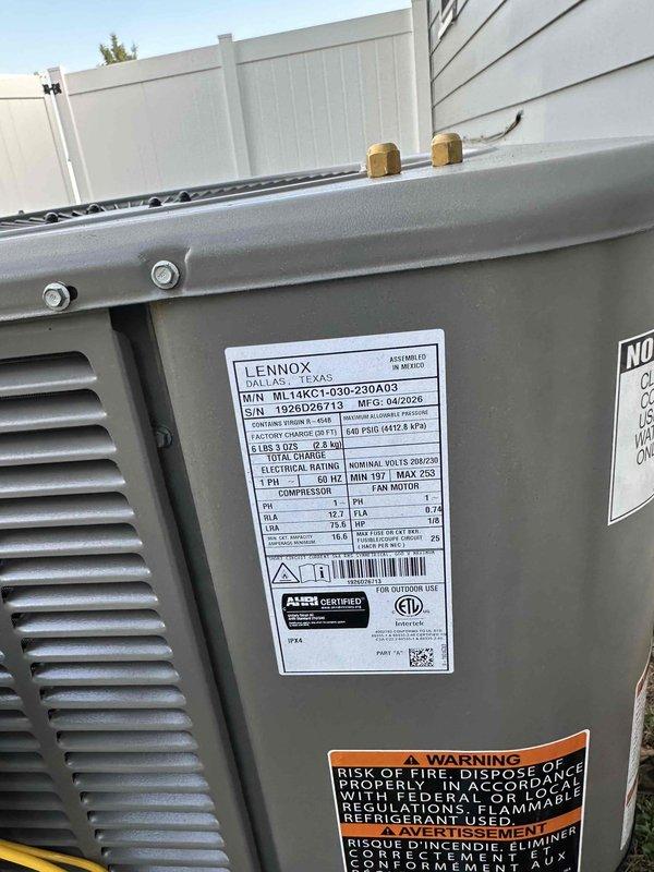 Completed installation of a 2.5-ton, 15.5 SEER Lennox air conditioning system with matching evaporator coil at residential property. The outdoor condenser unit (model 13ACX-LQ30-230A03) was positioned on a concrete pad against the building exterior with proper clearance for airflow and service access, electrical disconnect box mounted on siding with conduit run to unit, and refrigerant line set connected with insulated wrap at penetration point.