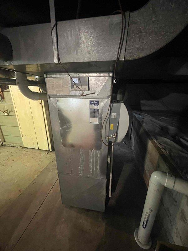 Conducted comprehensive assessment of existing HVAC system in basement installation for equipment replacement estimate. Customer reported current system operational but seeking replacement options. Evaluated gray metal furnace unit with associated ductwork, PVC condensate drainage system, and electrical disconnect box. Documented existing configuration including galvanized steel ductwork with horizontal ceiling runs, vertical air handler placement, and mechanical room layout adjacent to exposed brick wall. Photographed equipment specifications, manufacturer labels, and current installation conditions to provide accurate replacement recommendations and ensure proper sizing for new system installation.