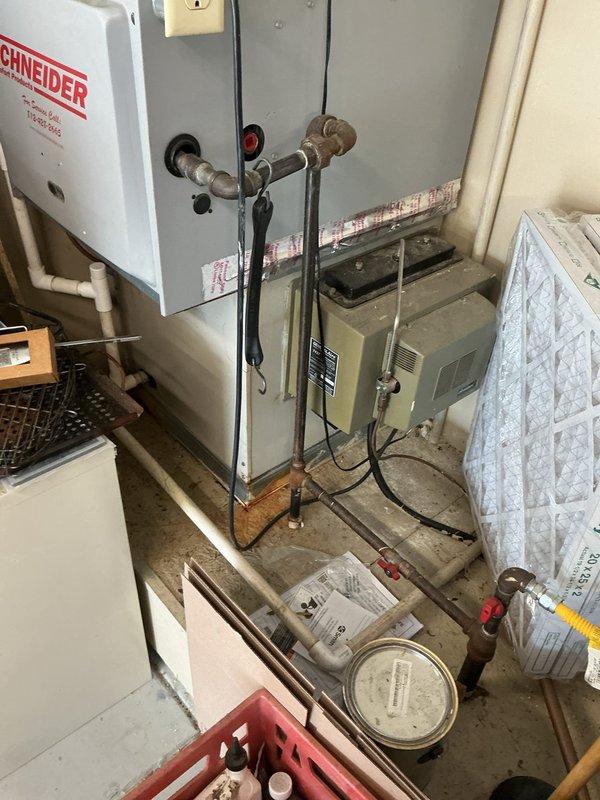Conducted comprehensive assessment of existing HVAC system for replacement estimate. Documented current equipment configuration including wall-mounted control board with visible circuit components, terminal connections, and wiring layout. Photographed mechanical room setup featuring existing heating unit on wooden platform, associated electrical panels, copper refrigerant lines, gas supply connections, and air filtration components to provide detailed scope for Green A+ rated replacement system proposal.