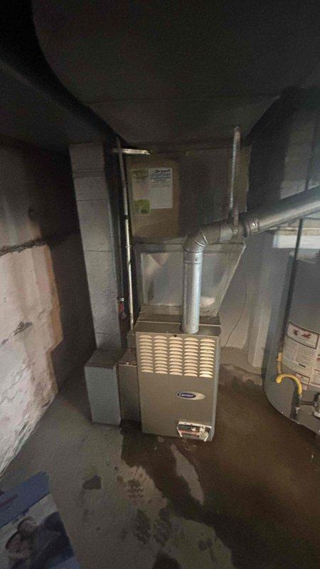 Conducted comprehensive HVAC replacement estimate for 18-year-old Carrier system including basement furnace installation and outdoor cylindrical condenser unit. Assessed condition of existing equipment showing signs of age and weathering, documented current system configuration with metallic ductwork, yellow gas line connections, and refrigerant lines running to exterior unit mounted on concrete pad with yellow block supports. Provided complete evaluation and replacement recommendations for aging heating and cooling system.