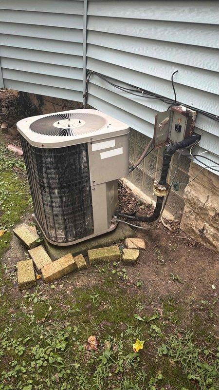 Conducted comprehensive HVAC replacement estimate for 18-year-old Carrier system including basement furnace installation and outdoor cylindrical condenser unit. Assessed condition of existing equipment showing signs of age and weathering, documented current system configuration with metallic ductwork, yellow gas line connections, and refrigerant lines running to exterior unit mounted on concrete pad with yellow block supports. Provided complete evaluation and replacement recommendations for aging heating and cooling system.
