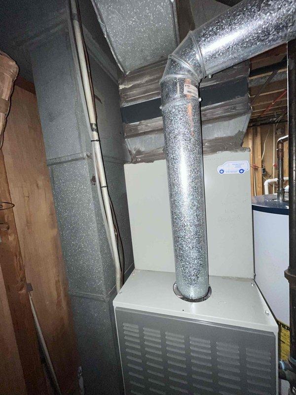 Conducted on-site evaluation for air conditioning condenser replacement at residential property. Assessed existing outdoor condenser unit positioned on concrete pad along exterior brick wall foundation, with electrical disconnect and conduit present. Inspected interior HVAC components including vertical and horizontal ductwork with reflective insulation in basement mechanical room. Documented current system configuration through photographs of outdoor condenser unit and indoor air distribution system. Provided estimate for new condenser installation to homeowner who was uncertain of existing unit's age and service history.