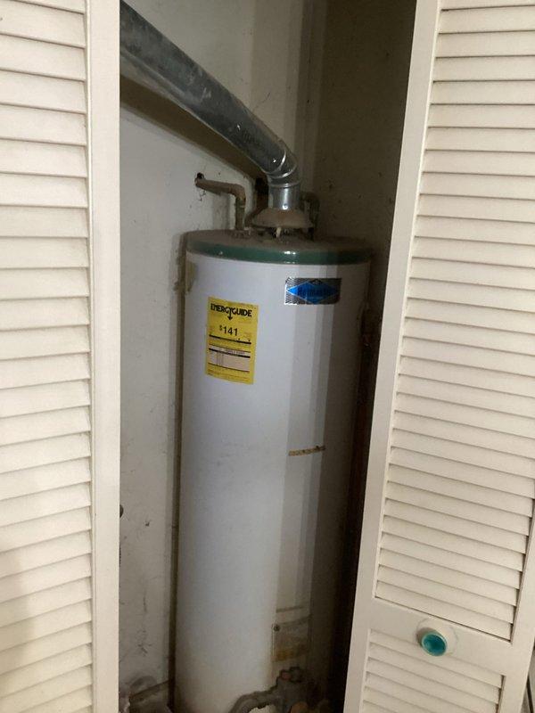 Conducted on-site evaluation for natural gas water heater replacement in residential property. Assessed existing 40-gallon tanked unit showing visible corrosion and rust staining on exterior surfaces. Unit located in narrow closet utility space with louvered bifold door access. Documented current installation configuration including gas supply line connections, copper water supply piping, and venting system with black insulated flue pipe. Measured available clearances within closet space to determine feasibility of installing larger capacity unit if desired. Evaluated utility room plumbing infrastructure and access points. Photographed existing equipment condition, pipe connections, and surrounding work area for estimate preparation. Provided professional assessment and recommendations for replacement options suitable for space constraints and customer scheduling requirements between 2-4 PM timeframe.