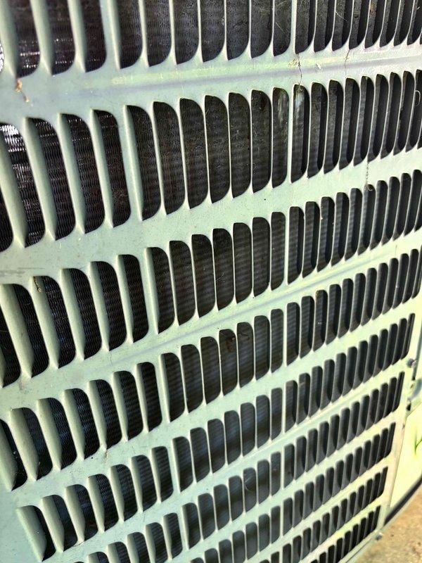 Responded to service call for outdoor condensing unit causing lights to dim and flicker throughout residence when system cycles on, accompanied by abnormal low humming noise. Upon inspection, identified hard start condition indicating compressor electrical draw issue affecting household electrical system. Evaluated condenser unit exterior condition, examined fin coil assembly for obstructions or damage, and assessed electrical disconnect and supply connections. Documented unit configuration and current operating symptoms with photographic evidence showing standard residential split system installation with adequate clearances. Recommended further electrical diagnostics to measure compressor amperage draw, capacitor testing, and potential contactor evaluation to resolve voltage drop and flickering issue.