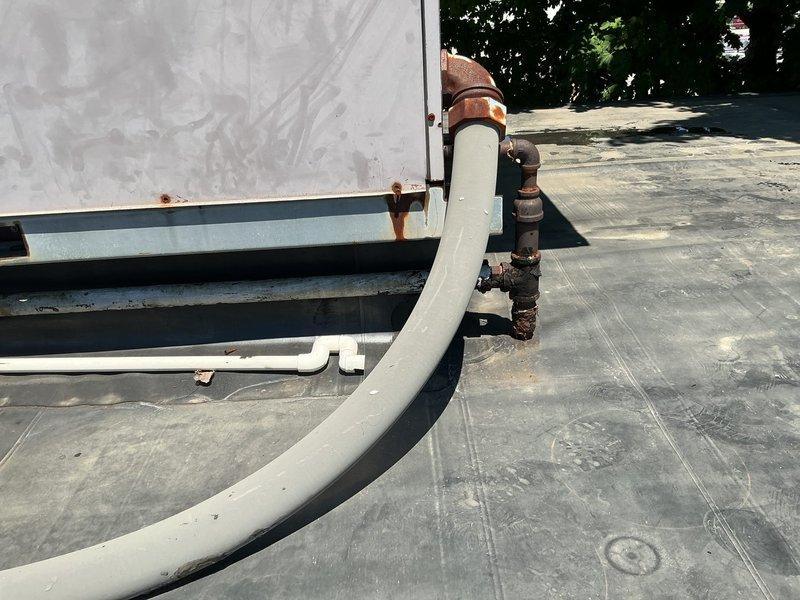 Completed follow-up site visit and documentation for rooftop HVAC system estimate. Photographed existing equipment conditions including heavily corroded piping, rusted metal fittings, and weathered PVC connections on commercial flat roof membrane. Documented rooftop unit placement, electrical disconnect box, support structures, and overall system accessibility for accurate proposal preparation.