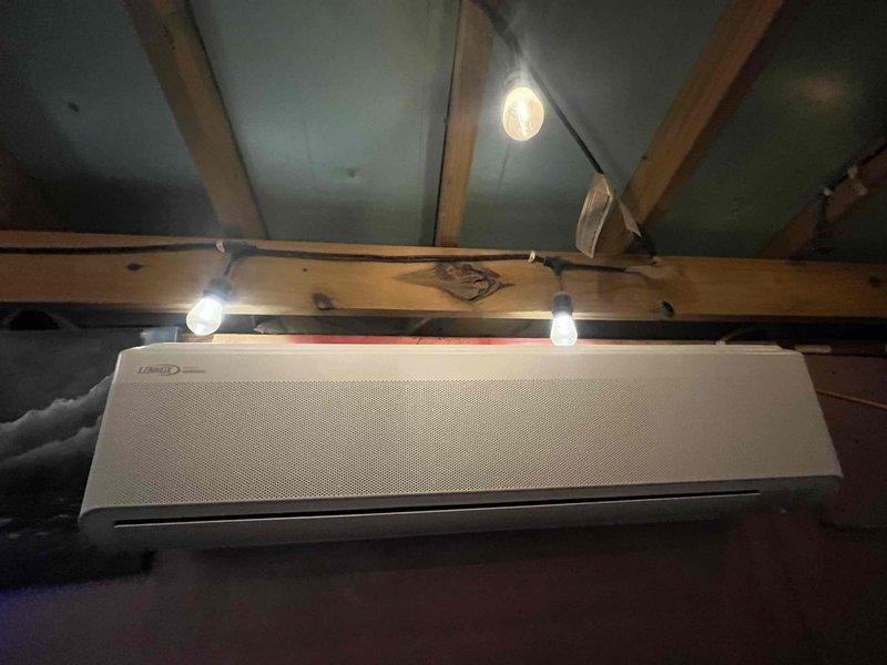 Completed installation of an 18,000 BTU ductless mini-split system in a residential property. Mounted outdoor condensing unit on concrete pad against exterior wood siding with proper refrigerant line sets and PVC condensate drain routing along the structure. Installed indoor air handler unit in attic space, securing it to structural joists with appropriate clearances for airflow and serviceability.