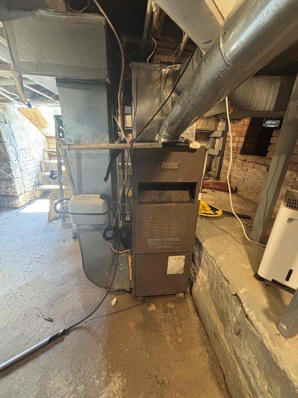 Conducted on-site evaluation for complete HVAC system replacement including 25-year-old air conditioning unit and furnace located in root cellar. Assessed existing upflow furnace installation with current ductwork configuration, measured clearances and dimensional requirements for new equipment installation. Documented existing system layout including plenum heights, coil positioning, and duct connections. Evaluated basement mechanical room conditions including exposed brick walls, concrete flooring, and accessibility for equipment removal and replacement. Photographed current furnace cabinet, supply ductwork, and surrounding utility infrastructure to determine optimal replacement specifications and installation requirements.
