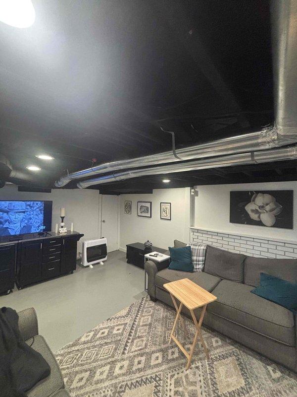 Completed follow-up site visit to assess and document ductwork installation in finished basement area. Verified metallic ductwork with reflective silver insulation is properly secured and routed across exposed black ceiling, with all joints fastened and sealed. System confirmed operational with adequate airflow distribution throughout living space.