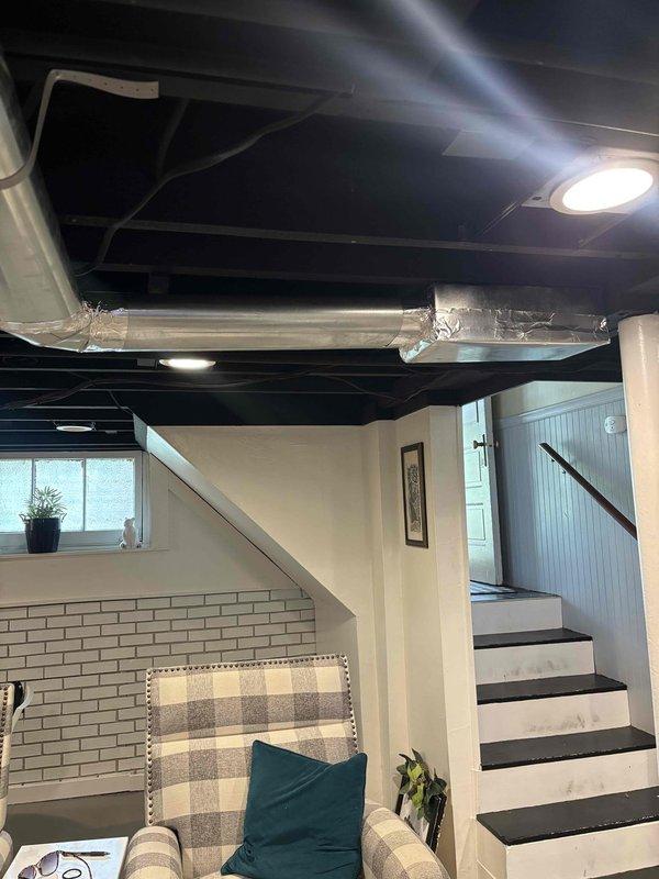 Completed follow-up site visit to assess and document ductwork installation in finished basement area. Verified metallic ductwork with reflective silver insulation is properly secured and routed across exposed black ceiling, with all joints fastened and sealed. System confirmed operational with adequate airflow distribution throughout living space.
