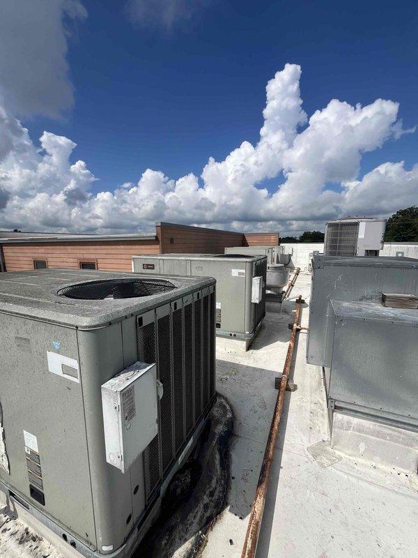 Conducted replacement estimate for 15-year-old rooftop packaged HVAC unit on commercial building with ladder access. Performed visual inspection and measurements of existing gray/green rooftop unit with fan grille and ventilation panels, documented equipment dimensions and electrical disconnect configuration. Assessed rooftop conditions including membrane surface and clearances around multiple existing HVAC units to provide comprehensive replacement system recommendations.