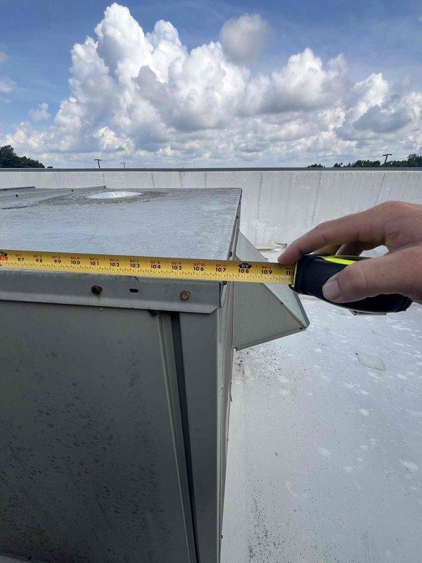Conducted replacement estimate for 15-year-old rooftop packaged HVAC unit on commercial building with ladder access. Performed visual inspection and measurements of existing gray/green rooftop unit with fan grille and ventilation panels, documented equipment dimensions and electrical disconnect configuration. Assessed rooftop conditions including membrane surface and clearances around multiple existing HVAC units to provide comprehensive replacement system recommendations.