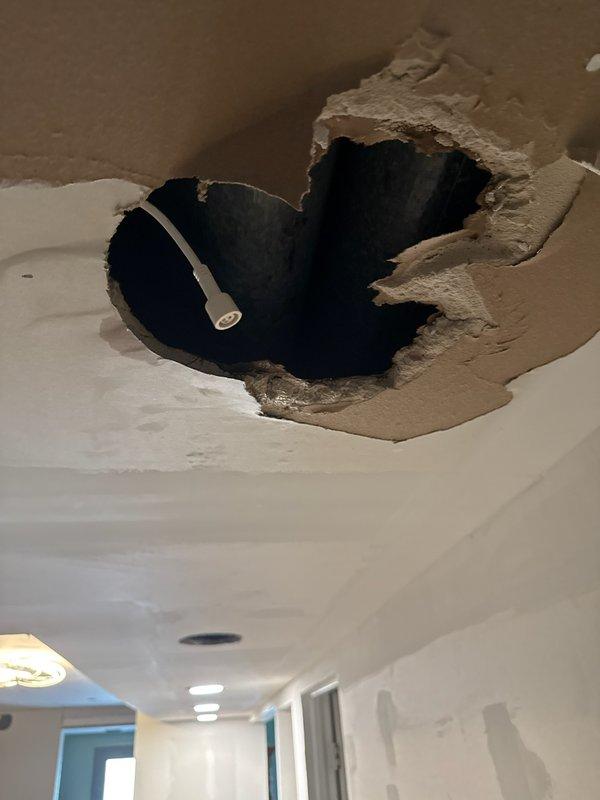 Responded to callback regarding water damage from condensate line issue. Documented extensive ceiling damage including compromised drywall with exposed cavity, visible electrical wiring, and water staining radiating from failure point. Photographed concrete floor showing black mold growth and moisture contamination beneath affected area. Customer reported damage to three light fixtures and surrounding drywall from condensate buildup that occurred during initial installation visit.