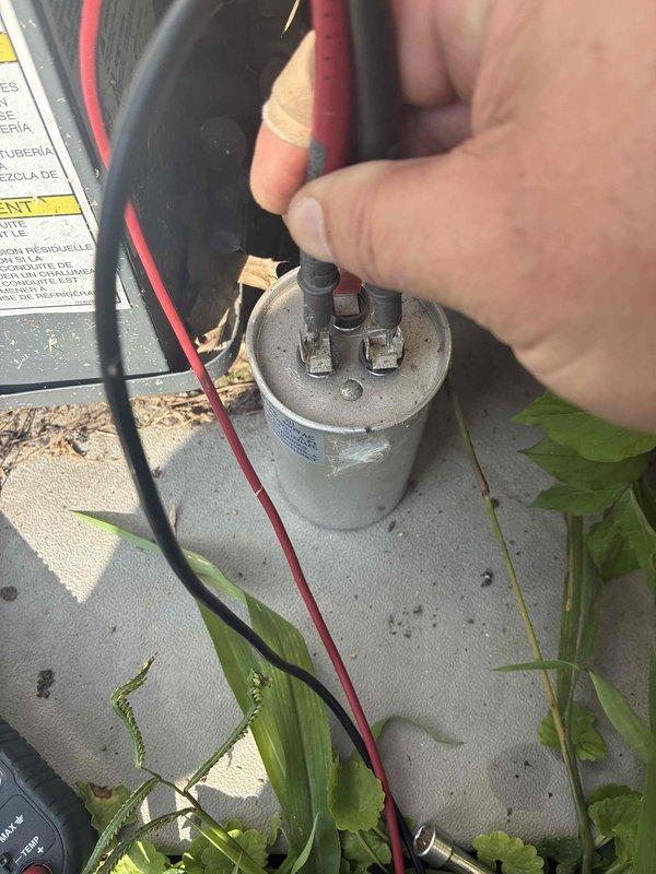 # Summary

Responded to no cooling complaint on 15-year-old AC system. Diagnosed failed capacitor causing reduced cooling performance, replaced defective component and restored normal operation.

# Work Performed

Arrived on site to address cooling system malfunction with room temperature air at supply registers. Customer reported recent decline in cooling performance. Condenser unit was running but system was not producing cool air. No refrigerant line icing observed upon arrival.

Performed visual inspection of outdoor condensing unit. Noted condenser coil had moderate fin damage with compressed sections affecting airflow efficiency. Vegetation growth near unit also restricting proper airflow. Condenser fan motor running but system not achieving proper cooling capacity.

Conducted electrical diagnostics on condensing unit components. Used multimeter to test capacitor voltage and capacitance values. Testing revealed capacitor reading significantly below manufacturer specifications, in