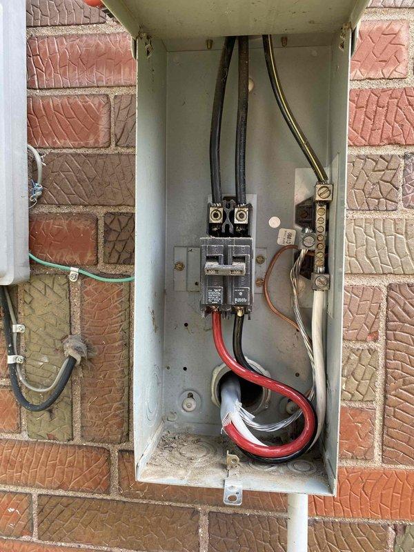 # Electrical Panel Service and Basement Wiring Installation

Serviced and upgraded outdoor electrical meter panel mounted on exterior brick wall. Installed new circuit breakers and routed additional electrical cables through panel enclosure, including heavy-gauge red conductor and multiple black service wires. Secured all cable entries with proper clamps and connectors, ensuring code-compliant installation. Added curved metal conduit connector to left side of panel housing for additional circuit routing. Verified grounding connections to existing vertical conduit system.

Completed basement electrical rough-in work, running multiple flexible conduit circuits through exposed ceiling joists. Installed new electrical panel on basement wall with proper mounting and clearance requirements. Added secondary electrical enclosure for circuit distribution. Installed new electrical outlet on lower wall section for basement utility service. All wiring secured to structural members per code require