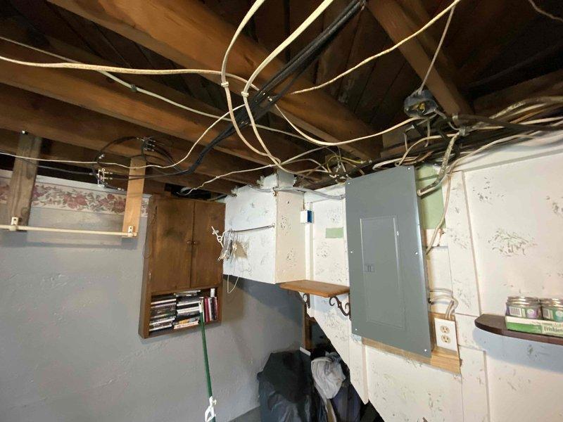 # Electrical Panel Service and Basement Wiring Installation

Serviced and upgraded outdoor electrical meter panel mounted on exterior brick wall. Installed new circuit breakers and routed additional electrical cables through panel enclosure, including heavy-gauge red conductor and multiple black service wires. Secured all cable entries with proper clamps and connectors, ensuring code-compliant installation. Added curved metal conduit connector to left side of panel housing for additional circuit routing. Verified grounding connections to existing vertical conduit system.

Completed basement electrical rough-in work, running multiple flexible conduit circuits through exposed ceiling joists. Installed new electrical panel on basement wall with proper mounting and clearance requirements. Added secondary electrical enclosure for circuit distribution. Installed new electrical outlet on lower wall section for basement utility service. All wiring secured to structural members per code require