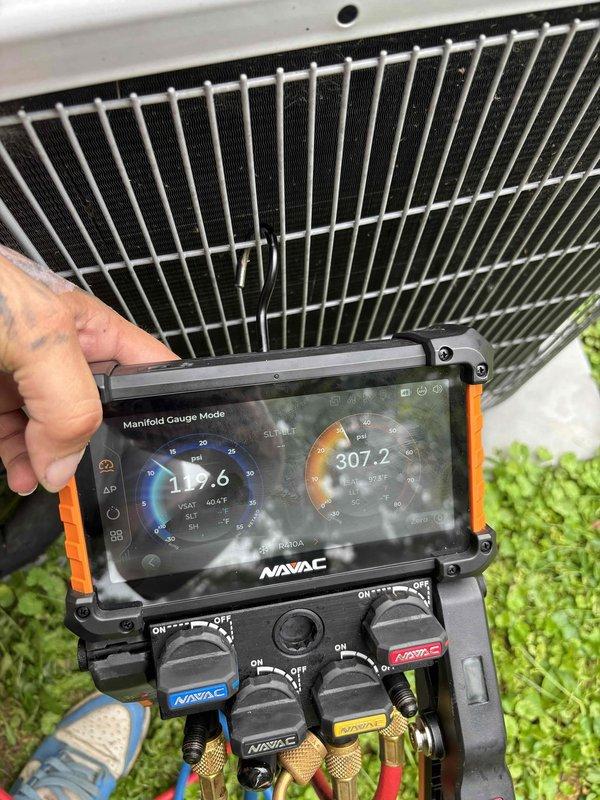 Responded to no cooling complaint on 5-6 year old residential split system. Upon arrival, found outdoor condenser unit humming but not operating properly, with system unable to maintain desired temperature. Performed diagnostic evaluation using digital manifold gauges, measuring system pressures at 117.6 PSI on low side and 307.2 PSI on high side. Pressure readings indicated refrigerant system imbalance contributing to inadequate cooling performance. Inspected condenser unit exterior condition, noting vegetation encroachment around concrete pad and equipment base requiring clearance maintenance for optimal airflow and operation.