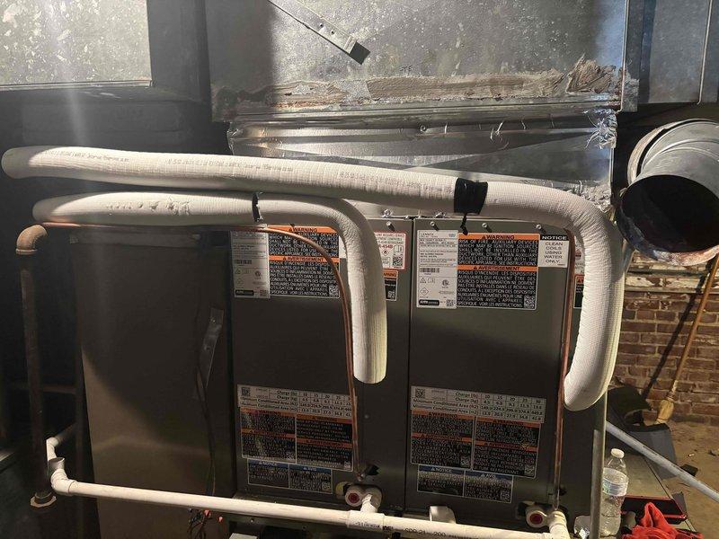 Completed installation of twinned 3-ton AC system in attic space, installing two 14-inch wide 3-ton cased evaporator coils on existing 80% efficiency furnaces. Fabricated and installed 20x12 return air drop measuring 55 inches with 1-inch filter rack for left-hand furnace. Connected refrigerant lines to both units, secured all piping with proper insulation and strapping, and verified system operation. All ductwork connections sealed and equipment positioned to accommodate existing 33.5-inch furnace height with 30-inch clearance to supply plenum.