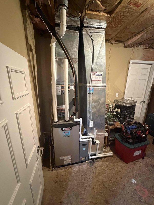 Completed full HVAC system installation including 3-ton 18 SEER air conditioning unit with dual outdoor condensers positioned on gravel pad against exterior brick wall. Installed new furnace/air handler and water heater in basement utility area with proper venting through white PVC piping and dark ductwork routed through ceiling joists. All units properly connected, tested for optimal performance, and system commissioned to manufacturer specifications.