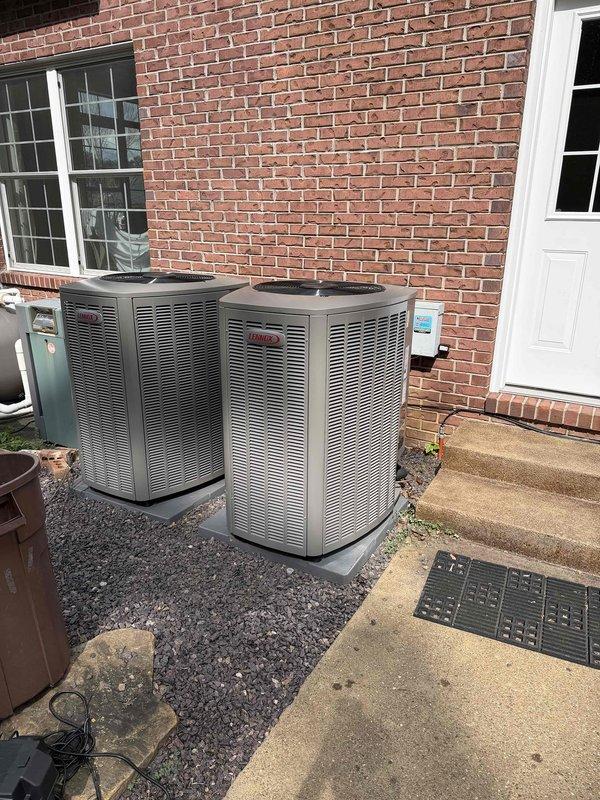 Completed full HVAC system installation including 3-ton 18 SEER air conditioning unit with dual outdoor condensers positioned on gravel pad against exterior brick wall. Installed new furnace/air handler and water heater in basement utility area with proper venting through white PVC piping and dark ductwork routed through ceiling joists. All units properly connected, tested for optimal performance, and system commissioned to manufacturer specifications.