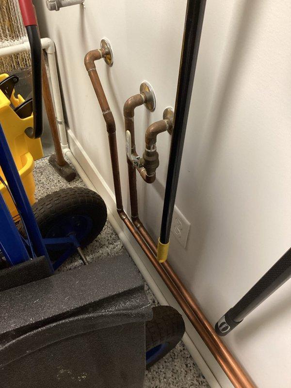 Responded to service call for tankless water heater not producing hot water. Performed diagnostic inspection of copper supply piping and connections in mechanical room area. Documented existing plumbing configuration including vertical copper lines with wall-mounted flanges and associated hydronic system components for follow-up assessment and repair recommendations.