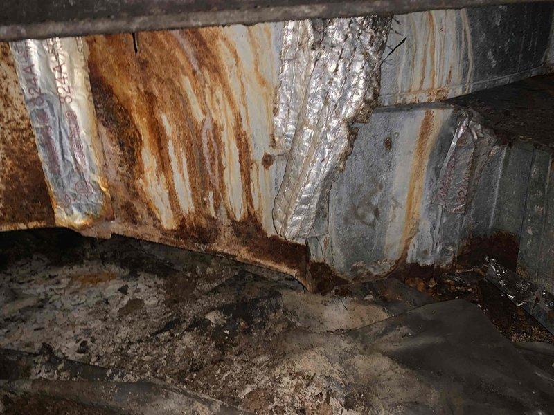 Responded to service call for insufficient airflow in two vertically aligned rooms on lower and upper levels of residence with 11-month-old HVAC system. Accessed crawlspace to inspect ductwork serving affected areas. Discovered extensive rust and corrosion on rectangular supply duct runs, with visible moisture damage and oxidation streaks indicating prolonged exposure to humidity. Documented deteriorated ductwork condition showing compromised structural integrity at joints and seams, despite previous attempts at sealing with metallic tape. Mapped duct layout connecting main trunk line to affected room registers. Identified airflow restriction likely caused by combination of corroded duct surfaces creating increased friction loss and potential separation or collapse at deteriorated connection points. Created diagram showing duct routing from main plenum through crawlspace to Spruce Hall area and stem room registers. Recommended duct replacement in affected sections due to advanced corro