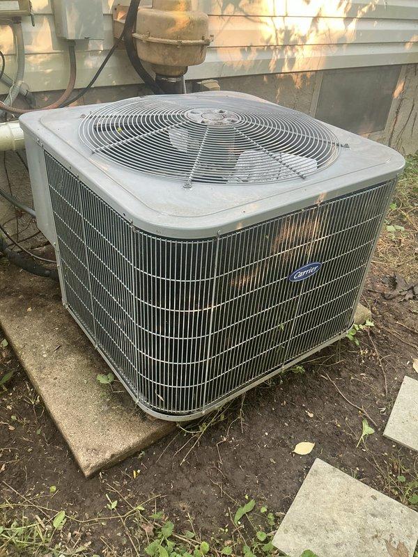 Responded to no-cooling call on 5-6 year old Carrier system with indoor temperature reading 79°F. Upon arrival, confirmed outdoor condenser fan motor was inoperative while compressor hummed, indicating failed condenser fan motor. Inspection of outdoor unit revealed severely deteriorated ductwork with extensive rust corrosion and structural failure, including large hole penetration in metal housing compromising system integrity. Documented equipment condition showing advanced oxidation and moisture damage throughout condensing unit cabinet and associated components.