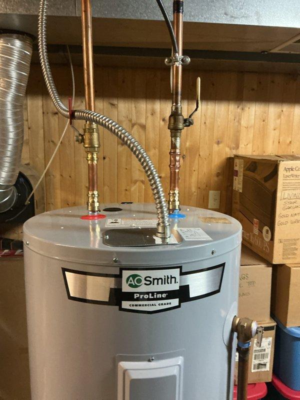 Completed installation of AO Smith ProLine commercial-grade electric water heater with 40-gallon capacity in basement utility area. Connected copper supply lines with brass fittings, installed hot and cold water connections with appropriate shut-off valves, and completed electrical wiring connections via flexible metal conduit. Unit properly positioned on concrete floor with all plumbing connections secured and tested for proper operation.