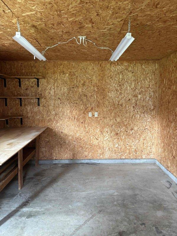 Conducted on-site evaluation for mini split system replacement in detached 19x12 backyard shop structure. Assessed existing conditions of unfinished workshop space with OSB walls and concrete flooring, documented electrical infrastructure including current outlet placement and lighting configuration, and evaluated exterior access points and clearances for outdoor condenser unit placement near landscaped areas adjacent to building siding.