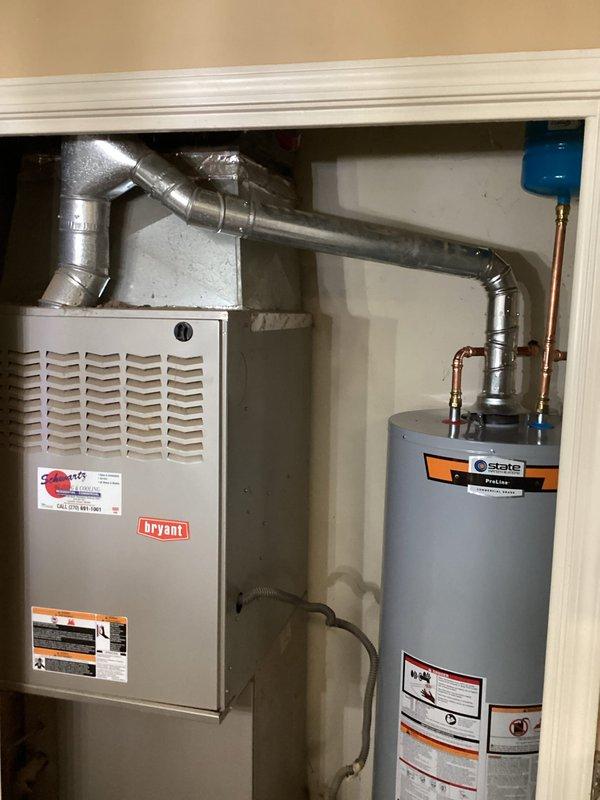 Completed installation of a 50-gallon State brand residential water heater in utility closet alongside existing Bryant HVAC furnace unit. Connected copper supply lines, gas piping, pressure relief valve, and flexible metal venting, ensuring all connections meet code requirements and manufacturer specifications for safe operation.