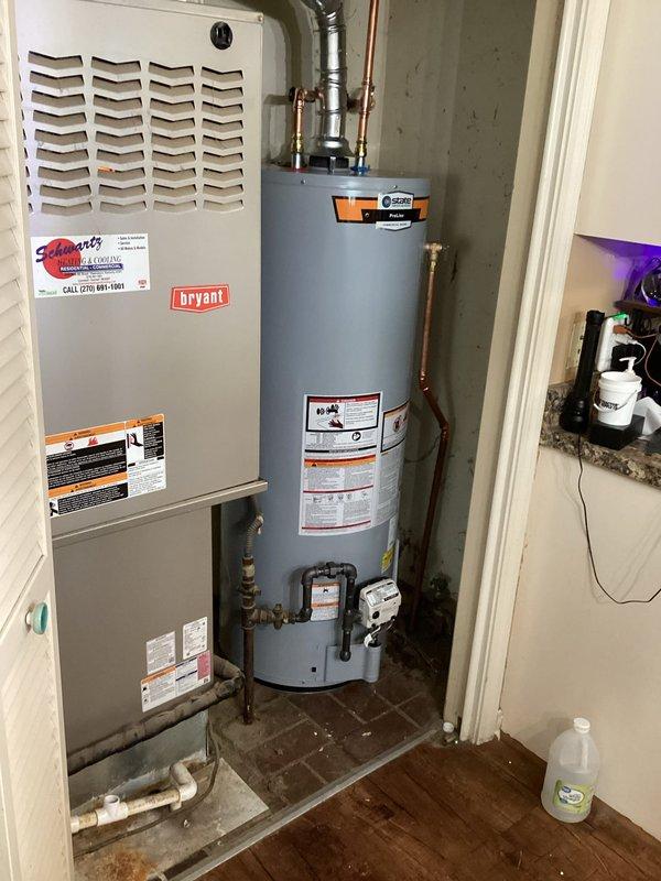 Completed installation of a 50-gallon State brand residential water heater in utility closet alongside existing Bryant HVAC furnace unit. Connected copper supply lines, gas piping, pressure relief valve, and flexible metal venting, ensuring all connections meet code requirements and manufacturer specifications for safe operation.