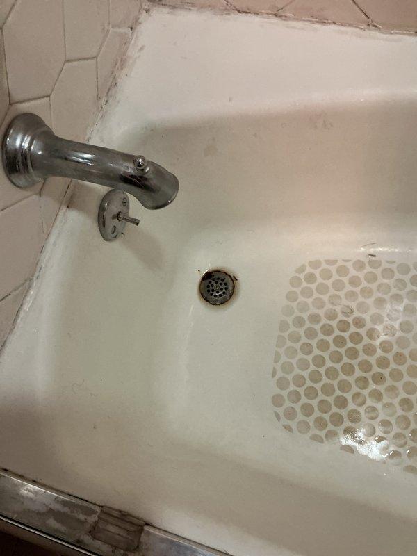 Responded to emergency call for active water leak in bathroom with water dripping onto light fixture below. Upon arrival, found leak originating from bathroom plumbing with water supply not shut off, creating potential safety hazard and ongoing property damage. Performed diagnostic inspection of bathtub area, identifying source of leak and assessing condition of existing plumbing fixtures including chrome spout, diverter valve, and drain assembly. Documented aging bathroom fixtures showing typical wear patterns, mineral deposits, and discoloration consistent with older plumbing systems. Shut off water supply to prevent further damage and completed assessment of affected areas to determine necessary repairs.