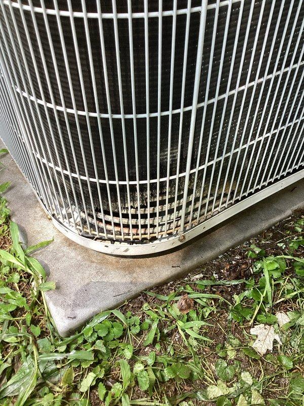 # HVAC Maintenance Summary

Completed Platinum Level preventive maintenance on single outdoor condensing unit. Performed comprehensive system inspection including visual assessment of condenser coil, protective grille, and mounting pad. Documented unit condition with photographic evidence showing exterior housing with vertical slat grille design and cylindrical configuration. 

Noted vegetation encroachment around concrete pad perimeter with weeds and grass growing near unit base. Observed normal weathering on exterior components including dirt accumulation and discoloration on lower portion of protective grille. Concrete mounting pad showed age-appropriate weathering with moisture staining. Internal components visible through grille appeared intact with no obvious damage to fins or coil structure.

System operational at time of inspection with no immediate mechanical concerns identified. Unit positioned on stable concrete foundation with adequate clearance for airflow. Recommended veg