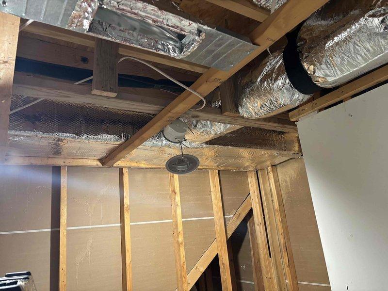 Completed comprehensive ductwork installation in attic space, including routing and securing flexible aluminum ductwork throughout the structural framework to support new HVAC system. Installed Trane heating and cooling unit with proper connections to the duct network, ensuring adequate airflow distribution. Added reflective insulation material along exposed sections and installed white rectangular air register with horizontal slats for optimal air delivery. All ductwork properly secured to wooden joists and beams, with connections sealed and insulated per manufacturer specifications for energy efficiency and system performance.