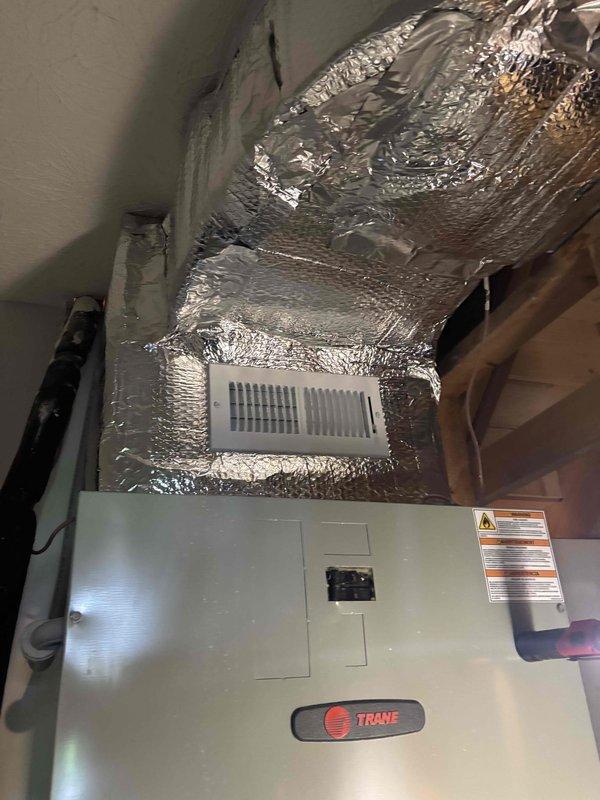 Completed comprehensive ductwork installation in attic space, including routing and securing flexible aluminum ductwork throughout the structural framework to support new HVAC system. Installed Trane heating and cooling unit with proper connections to the duct network, ensuring adequate airflow distribution. Added reflective insulation material along exposed sections and installed white rectangular air register with horizontal slats for optimal air delivery. All ductwork properly secured to wooden joists and beams, with connections sealed and insulated per manufacturer specifications for energy efficiency and system performance.
