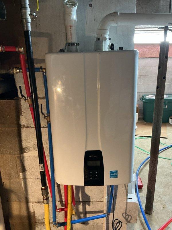 Successfully installed a Navien 240A2 tankless water heater system in the basement utility area, mounted on concrete block wall with proper venting through white PVC exhaust piping. Completed all hot and cold water supply connections using color-coded PEX tubing (red, blue, and yellow lines) with secure fittings to the unit's inlet and outlet ports. Configured digital control panel settings and verified proper operation of the tankless system. Unit is covered by a 5-year heat exchanger warranty and lifetime jacket warranty for the tankless components.