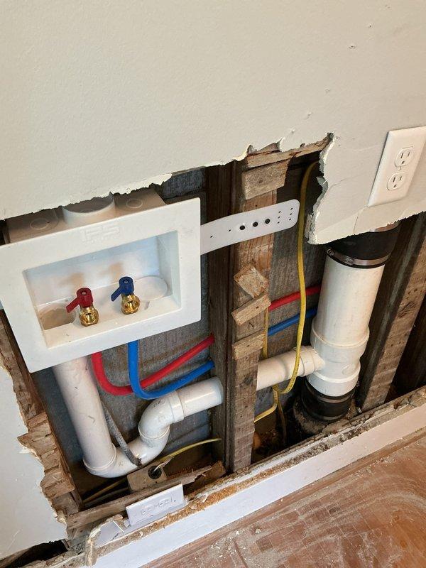 Installed washer supply box with two ball valve shut-offs and ran new water supply lines through interior walls to the box location. Ran drain line from existing 4-inch cast iron stack to washer box, requiring drilling through wood framing and cutting multiple access openings in drywall for pipe routing. Addressed multiple leaks on existing shower valve installation at threaded brass fittings and SharkBite connections, with customer acknowledging no warranty would be provided on owner-supplied parts or previously completed work. All PEX water supply lines were properly secured and connected with brass fittings. One-year warranty provided on washer box installation and associated plumbing work only.