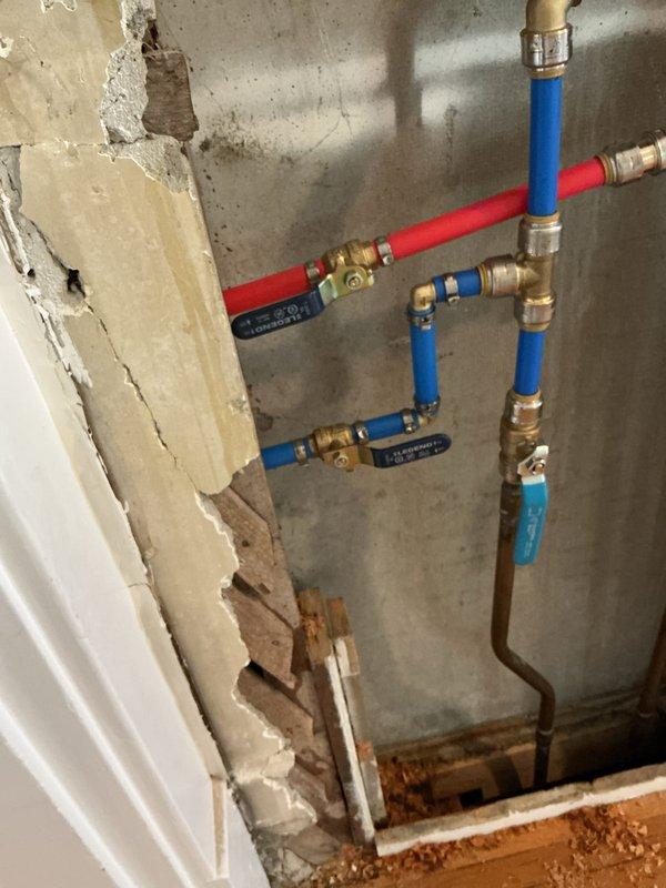 Installed washer supply box with two ball valve shut-offs and ran new water supply lines through interior walls to the box location. Ran drain line from existing 4-inch cast iron stack to washer box, requiring drilling through wood framing and cutting multiple access openings in drywall for pipe routing. Addressed multiple leaks on existing shower valve installation at threaded brass fittings and SharkBite connections, with customer acknowledging no warranty would be provided on owner-supplied parts or previously completed work. All PEX water supply lines were properly secured and connected with brass fittings. One-year warranty provided on washer box installation and associated plumbing work only.