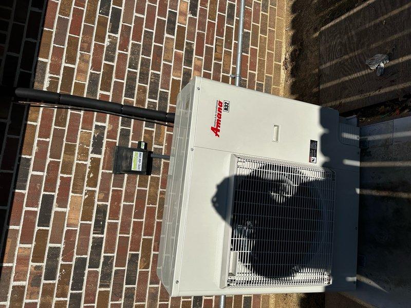 Completed full system installation consisting of indoor air handler unit in utility space and outdoor Amana condensing unit. Indoor work included mounting equipment on wooden joists, installing insulated refrigerant lines, and completing all necessary electrical connections. Outdoor unit was properly positioned on brick surface with line set connected to indoor components for a complete operational HVAC system.