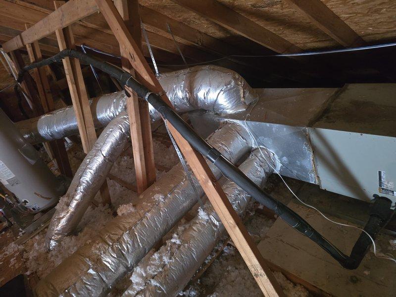 Conducted comprehensive assessment of 25-year-old residential HVAC system to determine replacement cost. Inspected exterior condensing unit located in side yard between brick wall and privacy fence, documenting equipment condition and installation configuration. Evaluated interior air handler unit and ductwork system in attic space, noting flexible metallic ductwork routing, insulation condition, and overall system accessibility for potential replacement considerations.