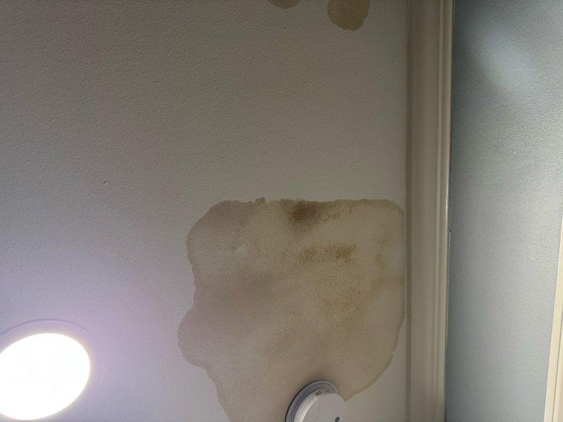 Responded to callback for secondary drain pan overflow causing ceiling water damage. Performed airflow measurement using manometer to verify system operation. Conducted internal plenum inspection with telescope camera to check for active water intrusion and confirm no water was overflowing the primary drain pan. Documented existing water damage to ceiling and wall, including brown staining and deterioration. Inspected drain pan area and found evidence of prolonged moisture exposure around drain line penetration through substrate. Verified proper drainage and system function to prevent further leakage.