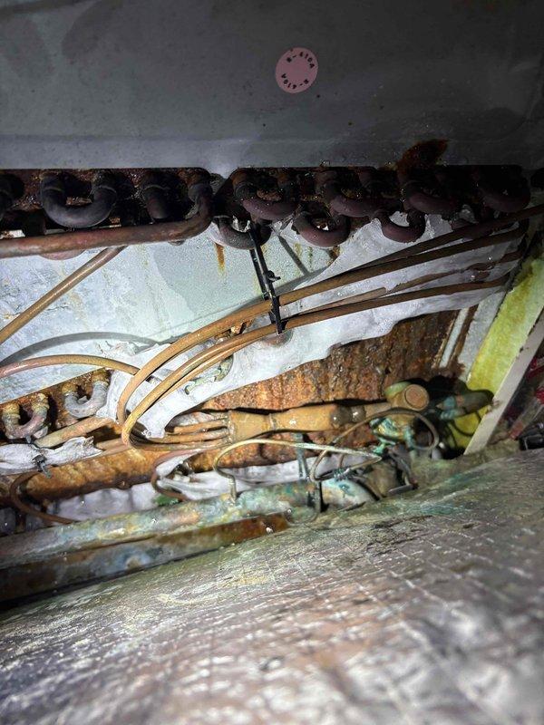 Responded to no cooling complaint on 2008 electric air conditioning system with gas heat. Customer reported thermostat displaying 77°F while set to 74°F, system blowing air but not cooling adequately, and drain pan overflow issues occurring intermittently over past two weeks. Upon arrival, system was turned off with thermostat fan set to ON per dispatch instructions.

Performed diagnostic evaluation of outdoor condensing unit and indoor evaporator coil assembly. Measured electrical parameters at condenser unit using clamp meter, recording 188.8 voltage and 50.02 Hz frequency, indicating proper power supply to equipment. Inspected outdoor unit fan motor operation and compressor function.

Conducted thorough inspection of indoor evaporator coil assembly, revealing extensive corrosion and rust deterioration on copper refrigerant lines and metal support components. Coil showed significant aging consistent with 16-year-old equipment, with visible oxidation on tubing and structural elements.