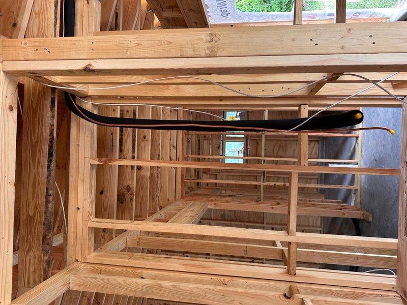 Completed installation of large-scale framing structure for residential construction project. The work involved installing dimensional lumber framing including ceiling joists, wall studs, rafters, and cross-bracing with proper metal brackets and hurricane ties at all critical connections. Routed electrical cables and wiring through the framing structure, securing black and gray cables along designated pathways with appropriate connectors and end caps. All structural members were aligned and secured according to building code standards, with plywood sheathing installed on ceiling joists. The installation provides a complete skeletal framework ready for the next phase of insulation and interior finishing work.