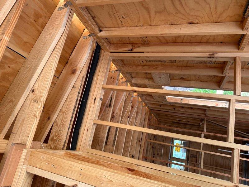 Completed installation of large-scale framing structure for residential construction project. The work involved installing dimensional lumber framing including ceiling joists, wall studs, rafters, and cross-bracing with proper metal brackets and hurricane ties at all critical connections. Routed electrical cables and wiring through the framing structure, securing black and gray cables along designated pathways with appropriate connectors and end caps. All structural members were aligned and secured according to building code standards, with plywood sheathing installed on ceiling joists. The installation provides a complete skeletal framework ready for the next phase of insulation and interior finishing work.
