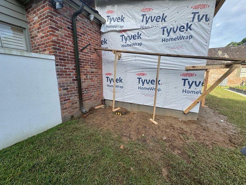 Conducted site assessment for residential addition or renovation project involving brick structure with new framed extension. Documented existing conditions including brick wall with mounted handrail, Tyvek HomeWrap installation on wooden framing, and construction staging area. Coordinated access arrangements for measurement collection while homeowner was unavailable. Photographed work area showing building envelope materials and structural framing to support scope development for upcoming construction phase.